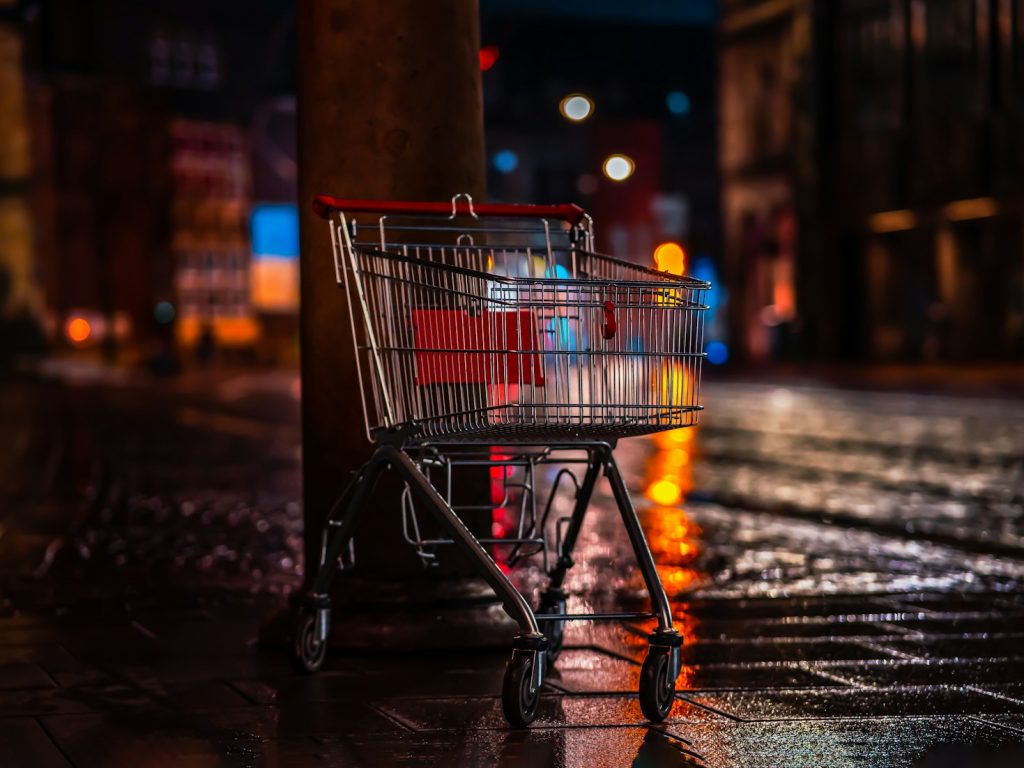 a shopping cart sitting next to a pole on a wet sidewalk
